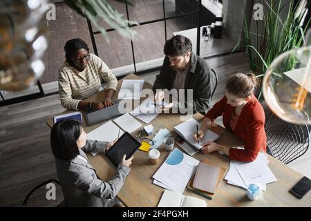 Vue de dessus d'un groupe multiethnique de personnes travaillant en collaboration tout en étant assis à une table de réunion dans l'intérieur du bureau graphique, espace de copie Banque D'Images