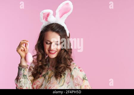 jeune femme en robe florale avec oreilles de lapin et oeuf de pâques isolé sur rose. Banque D'Images