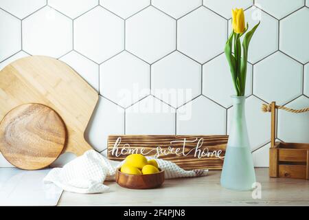 Vue de l'intérieur. Maison douce maison signe manuscrit sur le comptoir de cuisine à côté d'un bol en bois avec oeufs de Pâques et tulipe jaune dans vase et planches à découper Banque D'Images