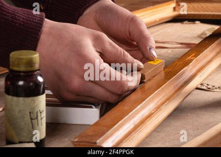 restauration de la porte, le maître sélectionne la couleur de la cire pour réparer les rayures et les éclats sur une ancienne porte en bois Banque D'Images