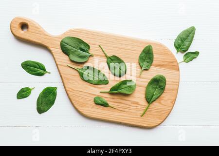 Planche à découper en bois avec des feuilles de salade verte d'épinards sur fond blanc. Concept de saine alimentation végétarienne. Photo de haute qualité Banque D'Images