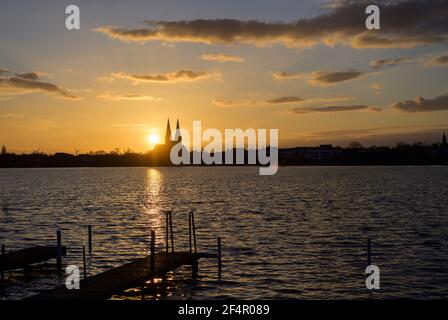 Neuruppin, Allemagne. 22 mars 2021. Le soleil se couche derrière le Ruppiner See et à côté des tours de l'église du monastère Saint Trinitatis. Credit: Soeren Stache/dpa-Zentralbild/ZB/dpa/Alay Live News Banque D'Images