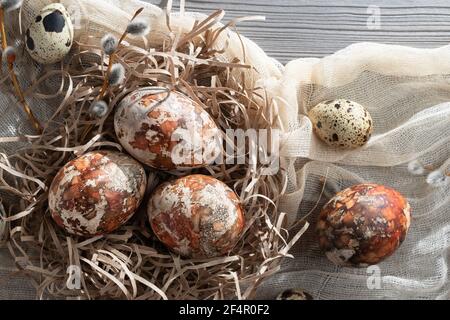 Composition Pâques - plusieurs œufs en marbre peints avec des teintures naturelles dans un nid en papier sur la table, vue du dessus. Banque D'Images