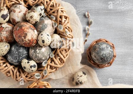 Composition Pâques - plusieurs œufs en marbre peints avec des teintures naturelles dans un nid et des paniers en osier, vue du dessus. Banque D'Images