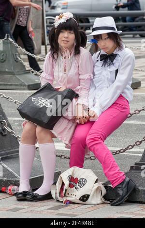 Deux jolies filles japonaises vêtues de main assise sur une clôture enchaînée à Harajuku, Tokyo, Japon Banque D'Images