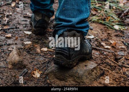 Jambes d'un touriste en bottes de randonnée sur une promenade en automne le long d'un sentier de montagne. Un homme en jeans bleus et en bottes de randonnée marche descend sur un sentier humide boueux. Banque D'Images