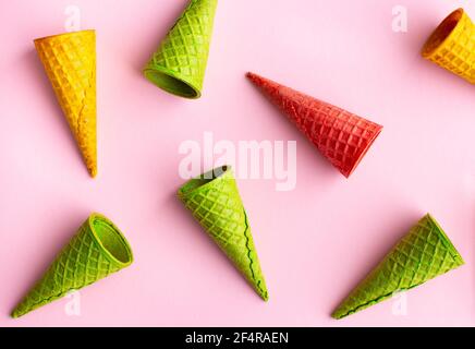 Cornets de crème glacée vides multicolores sur fond rose, plat. Banque D'Images