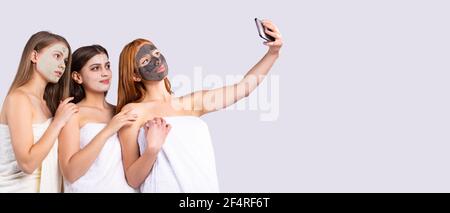 Bannière,format long.Trois jeunes femmes heureuses avec des masques en argile prennent un selfie.Espace publicitaire latéral. Banque D'Images