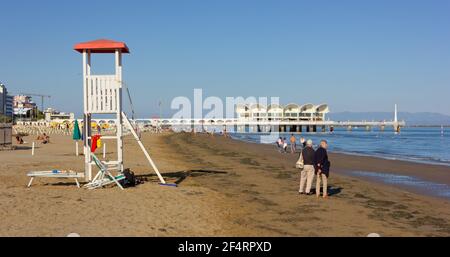 LIGNANO SABBIADORO, Italie - 30 septembre 2018 : personnes se promenant le long de la plage de Sabbiadoro, avec une tour de maître-nageur en premier plan Banque D'Images