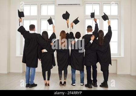 Vue arrière les élèves se tiennent dans une salle de classe avec leur dos à la caméra avec des planches de mortier surélevées. Banque D'Images