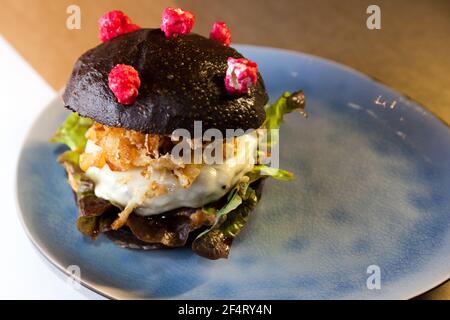 Cheeseburger Corona (antiCOVID) avec pain noir maison, laitue, oignon frit et fromage sur une assiette et une table en bois. Restaurant, Burger bar. Banque D'Images