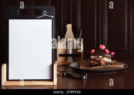 Photo d'un cadre en bois pour un menu ou une offre spéciale sur une table en bois sombre avec des couverts et un hamburger sur une assiette, fond sombre. Banque D'Images
