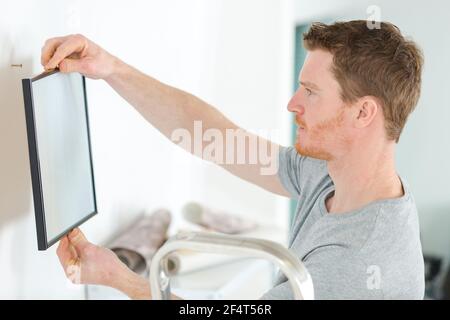 jeune homme mettant le cadre photo sur le mur Banque D'Images