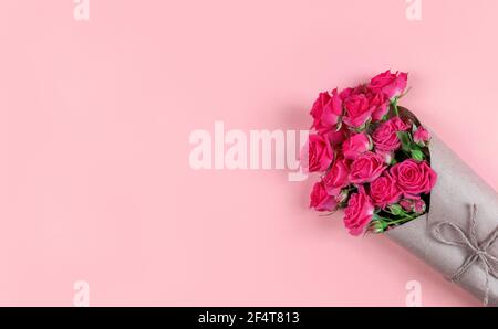 Bouquet de petites roses fleuries enveloppées dans du papier artisanal sur fond rose avec espace de copie. Banque D'Images