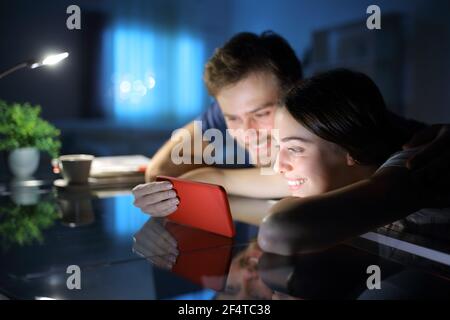 Couple heureux de regarder les médias ensemble sur smartphone dans le nuit à la maison Banque D'Images