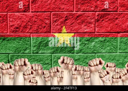 Des poings levés sur fond de drapeau représenté du Burkina Faso sur un mur de briques, un concept de force et d'unité. Banque D'Images