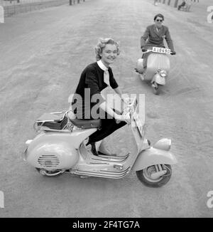 Vespa. Une marque italienne de scooter fabriqué par Piaggio. Le 23 avril 1946, Piaggio & C. S.p.A. a déposé un brevet pour "un cycle moteur avec un complexe rationnel d'organes et d'éléments avec corps combiné avec les garde-boue et le capot couvrant toutes les pièces mécaniques". Peu de temps après, la Vespa a fait sa première apparition publique. La jeune fille sur la Vespa est la gagnante suédoise du concours de beauté Anita Sohlman et l'année est 1955. Elle apprend à conduire. Banque D'Images