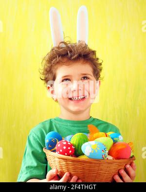 Petit garçon mignon avec des oreilles de lapin sur sa tête tenant Un panier en osier avec des œufs de Pâques peints à la maison Banque D'Images