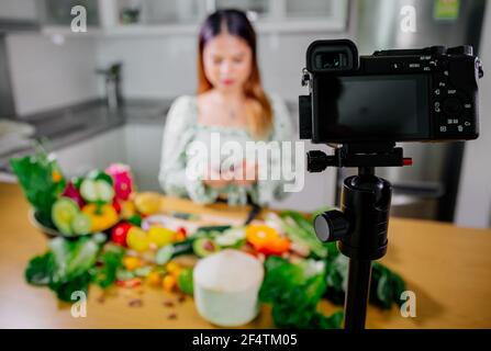 Femme asiatique blogueur ou créateur de contenu de cuisine et d'enregistrement caméra vidéo. Montrant la nourriture saine tout en enregistrant avec l'appareil photo dans la cuisine. Banque D'Images