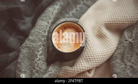 Une tasse noire remplie de café chaud et revigorant à la cannelle se tient parmi les pulls en laine chaude préparés pour les jours froids de l'hiver. Hygge. Banque D'Images