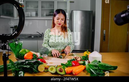 Femme asiatique blogueur ou créateur de contenu de cuisine et d'enregistrement caméra vidéo. Montrant la nourriture saine tout en enregistrant avec l'appareil photo dans la cuisine. Banque D'Images