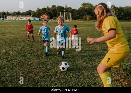 Enfants jouant au football à l'extérieur. Gardien de but de fille attrapant le ballon de football à la compétition amateur. Banque D'Images