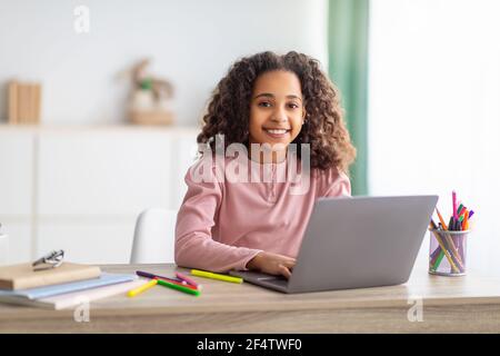 Apprentissage en ligne. Fille afro-américaine étudiant sur ordinateur portable apprenant à la maison et souriant à l'appareil photo Banque D'Images