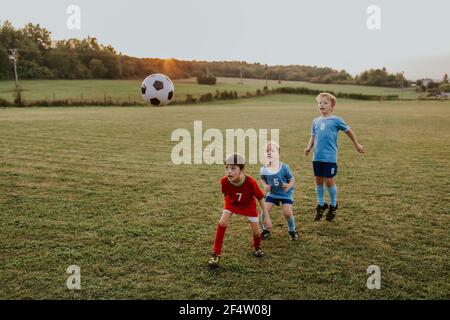 Enfants jouant au football amateur. Sur toute la longueur des jeunes garçons vêtues de robes de football ayant une tête de lit amusante sur le terrain. Banque D'Images