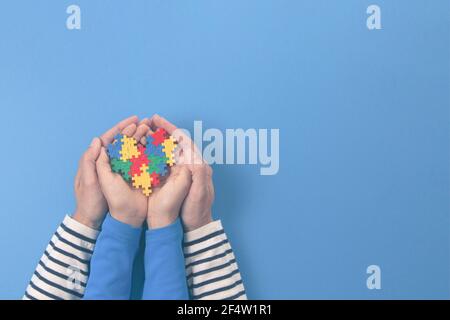 Concept de journée mondiale de sensibilisation à l'autisme. Les mains des adultes et des enfants tiennent le cœur du puzzle sur un fond bleu clair Banque D'Images
