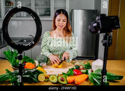 Femme asiatique blogueur ou créateur de contenu de cuisine et d'enregistrement caméra vidéo. Montrant la nourriture saine tout en enregistrant avec l'appareil photo dans la cuisine. Banque D'Images