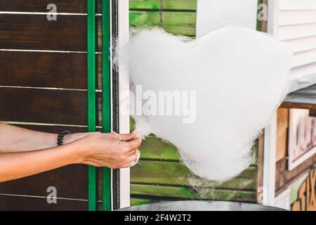 Les mains de la fille sont tenues sur un bâton et font des bonbons de coton sur le fond de la rue. Banque D'Images