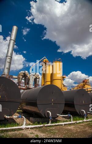 Usine de mélange d'asphalte. Silos de mélange jaunes et cheminée de fumée grise. Ciel bleu avec des nuages de beauté. Banque D'Images