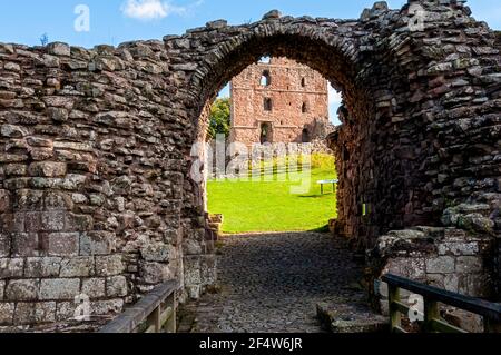 Les ruines d'une passerelle en pierre dans les murs-rideaux Du château de Norham en dessous d'une pente raide couverte d'herbe menant au mur intérieur de la paroisse et à la grande tour Banque D'Images