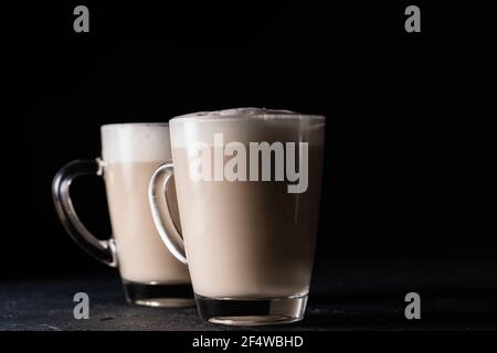 Deux tasses de thé Chai Latte, boisson chaude au thé avec lait mousse sur fond noir foncé Banque D'Images