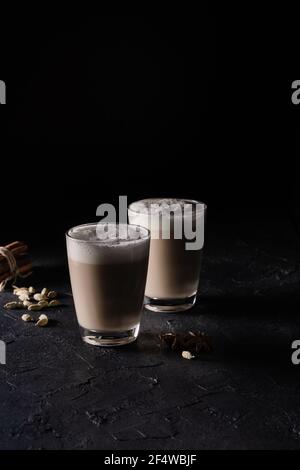 Deux tasses de thé Chai Latte, boisson chaude au thé avec lait mousse sur fond noir foncé Banque D'Images