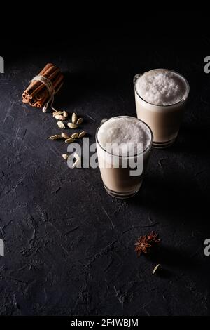 Deux tasses de thé Chai Latte, boisson chaude au thé avec lait mousse sur fond noir foncé Banque D'Images