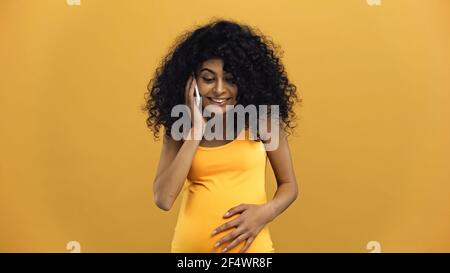 Femme hispanique enceinte parlant au téléphone cellulaire isolée sur jaune Banque D'Images