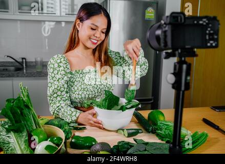 Femme asiatique blogueur ou créateur de contenu de cuisine et d'enregistrement caméra vidéo. Montrant la nourriture saine tout en enregistrant avec l'appareil photo dans la cuisine. Banque D'Images