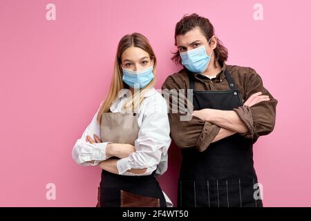 Les serveurs sérieux et confiants se tiennent avec les bras repliés, prêts à servir les clients pendant COVID-19, portrait de l'homme et de la femme dans l'isolat de masque de protection médicale Banque D'Images
