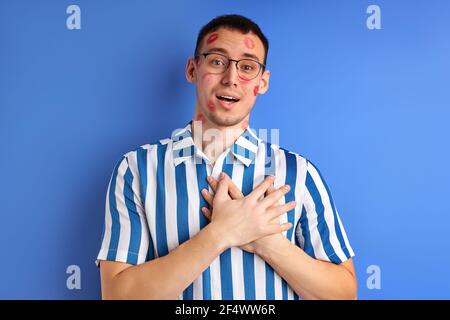 Homme inspiré avec des traces de Kiss sur la joue tenant les mains sur la poitrine, Caucasien Guy en Blue rayed shirt regardant la caméra parlant, exprimant l'amour Banque D'Images