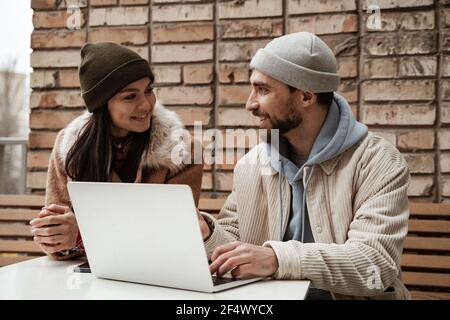 joyeux freelance dans des chapeaux beanie regardant les uns les autres près ordinateur portable Banque D'Images