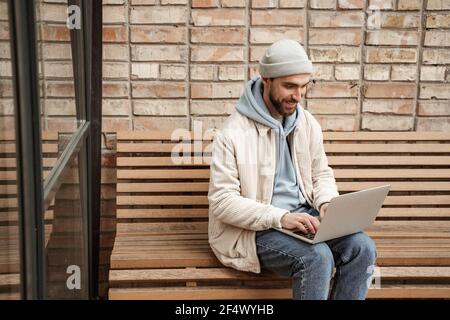 bonne freelance à barbe dans un bonnet beanie avec ordinateur portable assis sur banc Banque D'Images