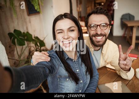 femme joyeuse qui colle la langue près de l'homme montrant le signe de la paix Banque D'Images