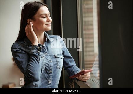 femme heureuse dans les écouteurs sans fil écouter de la musique et tenir le smartphone Banque D'Images