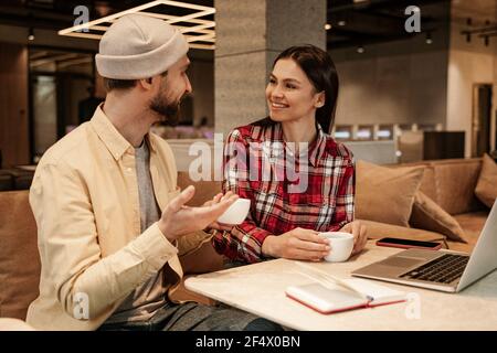 femme gaie regardant l'homme dans un bonnet beanie avec une tasse de café Banque D'Images