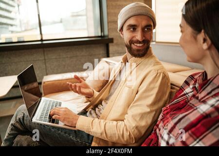 joyeux freelancer barbu dans beanie chapeau gestante près de l'ordinateur portable et femme Banque D'Images