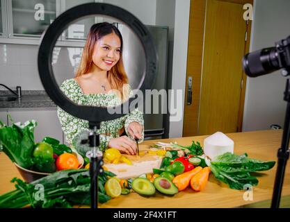 Femme asiatique blogueur ou créateur de contenu de cuisine et d'enregistrement caméra vidéo. Montrant la nourriture saine tout en enregistrant avec l'appareil photo dans la cuisine. Banque D'Images