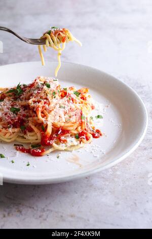 Fourchette retirer quelques pâtes d'une assiette de spaghetti frais avec sauce tomate, parmesan et persil haché. Banque D'Images