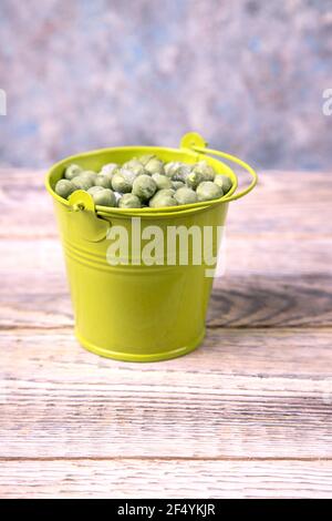 Pois verts congelés dans un seau vert sur une table en bois. Banque D'Images