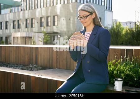 Femme d'affaires expérimentée et concentrée qui déjeune en plein air Banque D'Images